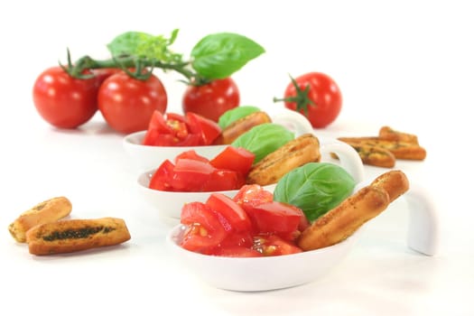 Grissini with tomato pieces and basil in appetizer spoons on white background