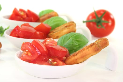 Grissini with tomato pieces and basil in appetizer spoons on white background