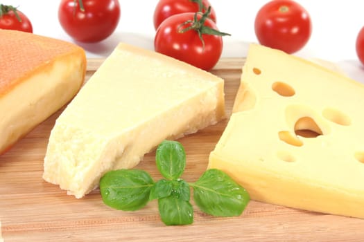 a selection of cheeses with tomato and basil on a wooden board