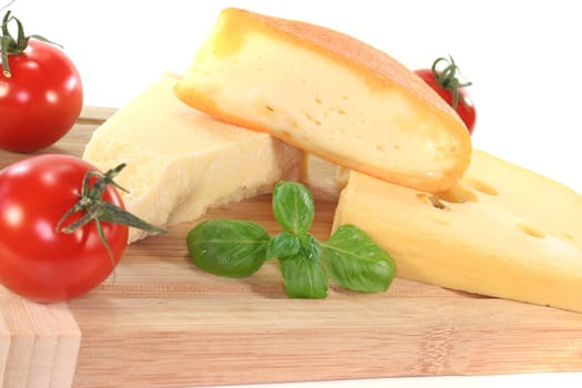 a selection of cheeses with tomato and basil on a wooden board