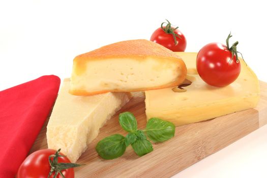 a selection of cheeses with tomato and basil on a wooden board