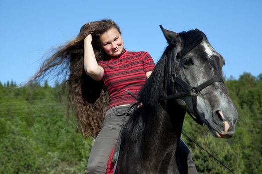 A girl with flowing hair on a black horse in a forest