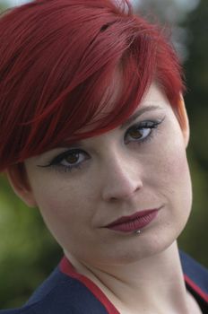 Portrait of a girl with red hair, piercing on lower lip, serious expression.