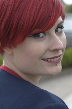 Portrait of a girl with red hair, piercing on lower lip, smile expression.