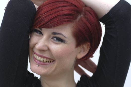 Portrait of a girl with red hair, piercing on lower lip, laughing expression and arms around head.