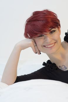 Portrait of a girl with red hair, piercing on lower lip, and tattoos on chest and shoulders, happy expression.