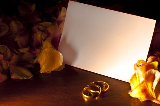 White card with wedding rings, surrounded by rose petals