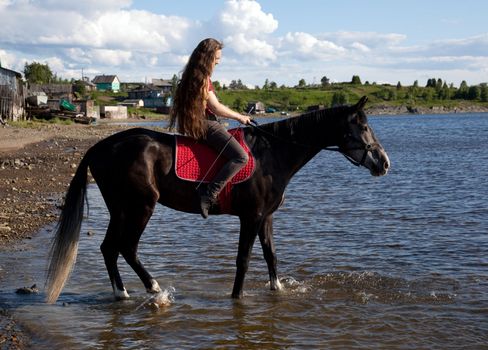 A girl with flowing hair on a black horse rides to swim
