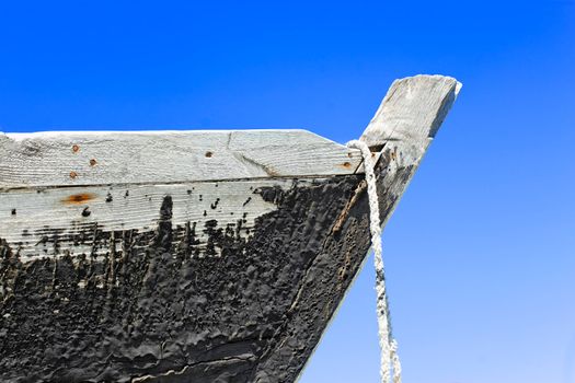 The prow of the old wooden boat with a tarred surface against blue sky
