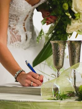 Bride with wedding bunch of flowers (bouquet) signing marriage lines (certificate).