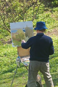 Senior man painting in a hat.