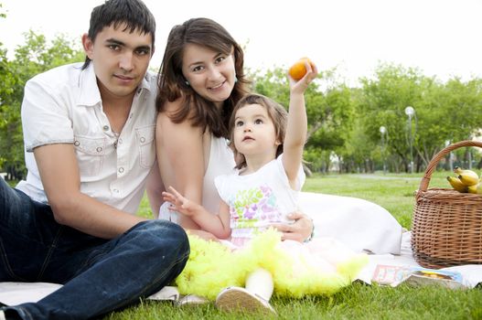The husband, the wife and the child sit on a coverlet in park