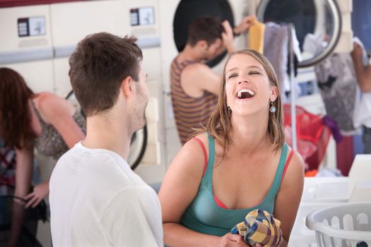 Happy young woman with boyfriend laughs out loud in the laundromat 