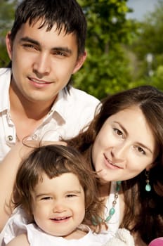 The husband, the wife and the child sit on a coverlet in park