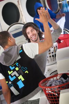 Happy young man gives high five to his friend in a Laundromat