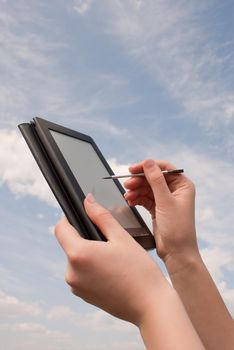 Hands hold electronic book reader against blue sky
