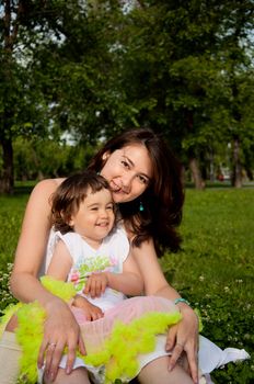 Mum embraces the daughter, sitting on the grass