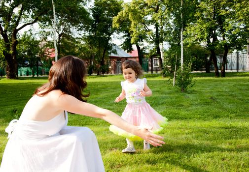 The daughter runs towards to mum on a grass