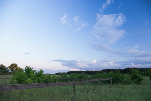 Meadow with fence and blue sky.