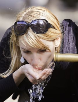 Young lady drinking tap water from the fountain in the city park on a hot summer day.