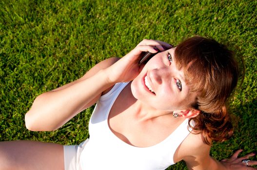 portrait of young woman talking on phone, green grass background