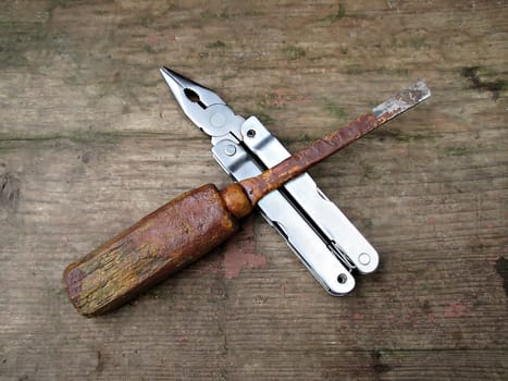 Old screwdriver and new pliers laying on a wooden board