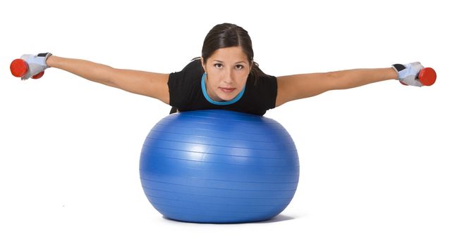 Young woman doing an exercise with barbells and a fitness ball