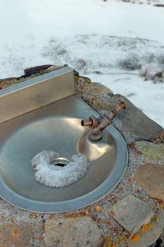 a frozen outdoor water tap against a winters snow background