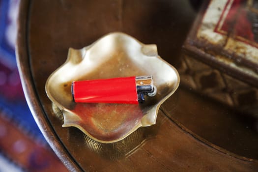brass ashtray red cigarette lighter, ornamental case on a round glass inlaid occasional table