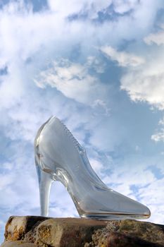 a glass slipper on a stone surface with a cloudy blue sky background