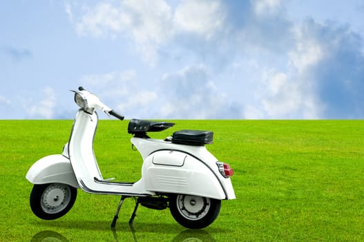 White vintage motorbike parking on the grass with nice cloudy sky