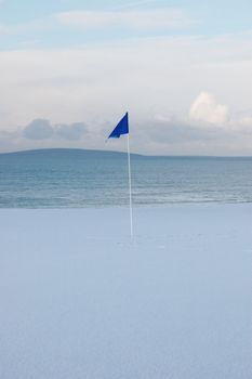 a snow covered links golf hole in ireland in winter weather with blue flag