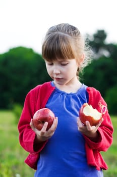 little girl eating apples in a meadow. healthy nutrition concept.