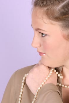 Beautiful teenage female against purple background, wearing pearls 