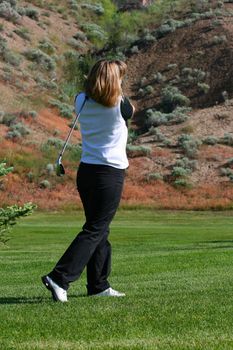 Blond female golfer playing an Iron shot
