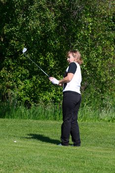 Adult female golfer playing an iron shot from the fairway