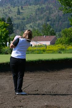 Adult female golfer playing a shot out of the bunker