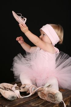 Blond toddler wearing a tutu holding Ballet shoes 