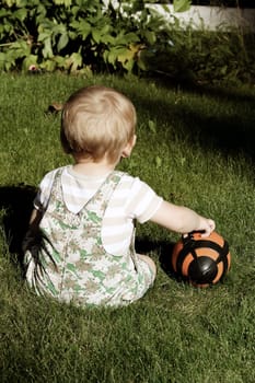 Cute blond baby boy sitting outside in the garden