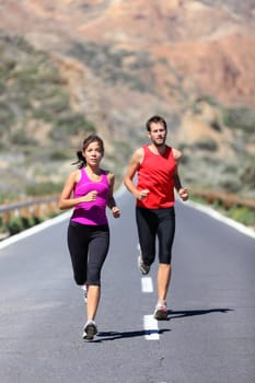 Couple running. Two runners training for marathon run outdoors on road in beautiful landscape. Man Caucasian runner and Asian woman runner.