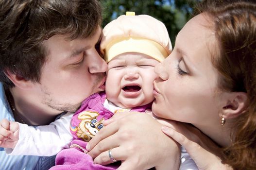 Father and mother kissing a child, the child is crying and sad