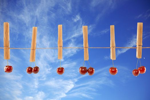 Sweet red cherries and clothes line on a sky background