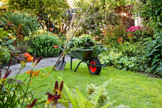 Evening after work in summer garden with wheelbarrow, shovel and rake - horizontal