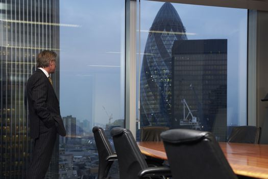 Senior business man standing in boardroom alone looking out of window of view of city