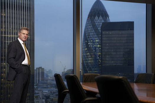 Business man standing next to table in boardroom looking at camera