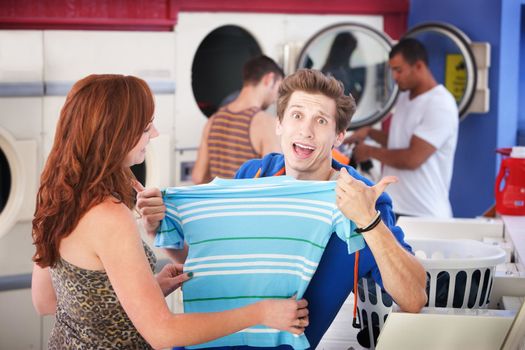Unhappy man with girlfriend holds a shrunken t-shirt in laundromat