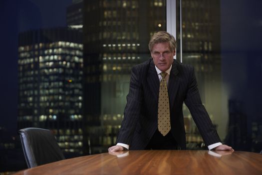 Senior businessman leaning on boardroom table looking at camera