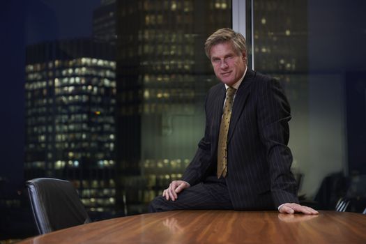 Business man sitting on table in boardroom looking at camera