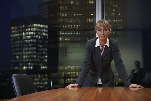 Senior Business woman leaning on table in boardroom looking at camera