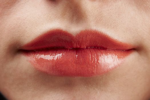 Close-up of womans lips with red glossy lipstick